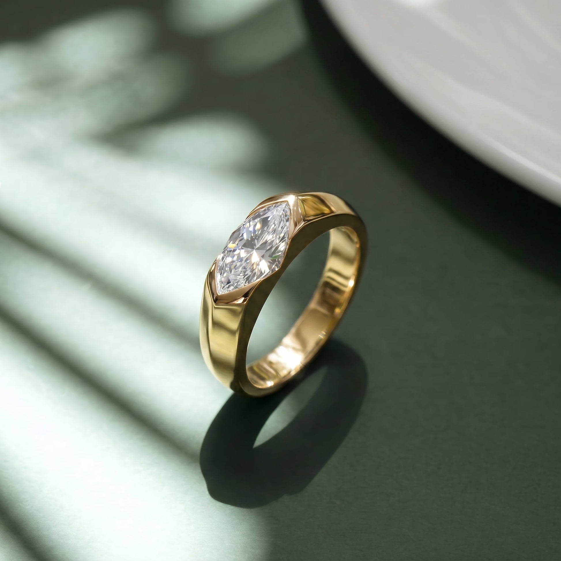 Side angle of gold-plated east-west solitaire engagement ring casting shadow on dark green background