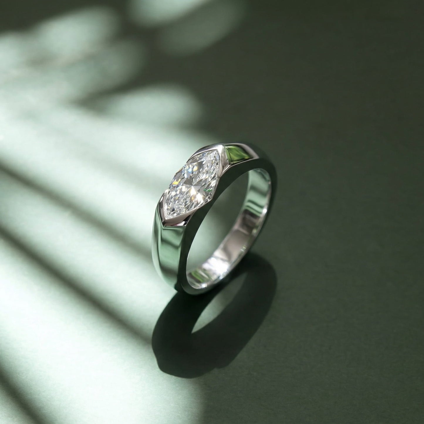 Side angle of platinum-plated east-west solitaire engagement ring casting shadow on dark green background