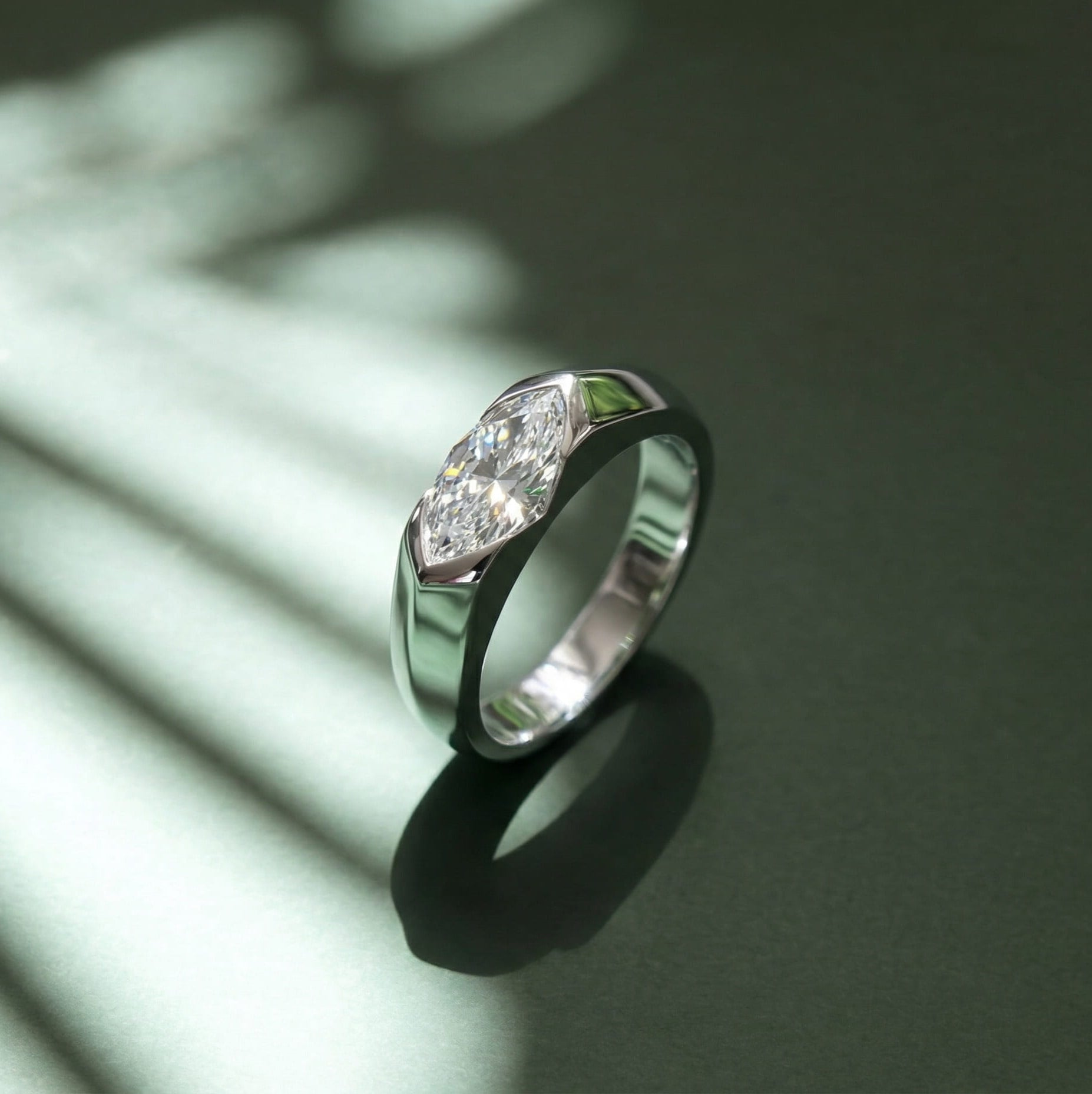 Side angle of platinum-plated east-west solitaire engagement ring casting shadow on dark green background